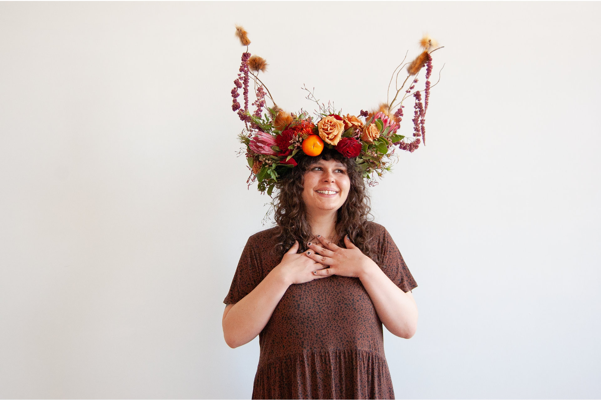 Woman smiling with hands on her heart, wearing a floral headdress.